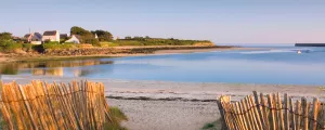 Accès à la plage entre des ganivelles vers une anse bretonne et des maisons au bord de l'océan au loin
