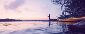 Pêcheur les pieds dans l'eau proche d'une rive d'un étang au lever du soleil