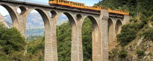 Petit train jaune sur un aqueduc au milieu des montagnes des Pyrénées