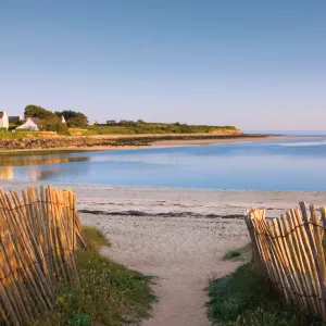 Accès à la plage entre des ganivelles vers une anse bretonne et des maisons au bord de l'océan au loin