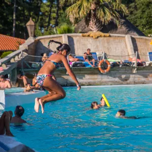 Enfant qui saute dans l'eau de la piscine chauffée au camping le Vieux Port à Messanges dans les Landes 