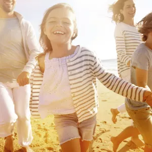 Famille se tenant par la main et petite fille souriant sur la plage les pieds dans le sable