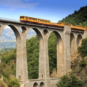 Petit train jaune sur un aqueduc au milieu des montagnes des Pyrénées