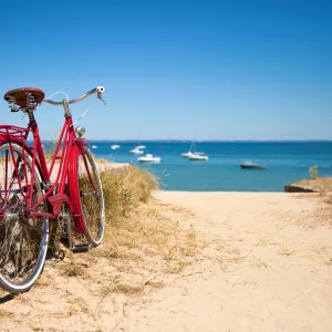 Vélo posé dans le sable face à une plage avec des bateaux amarés