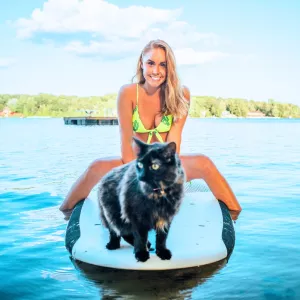 Femme et son chat sur une planche de paddle, au cœur d'un lac paisible, dans un camping accueillant les animaux. Une expérience unique de détente en pleine nature.