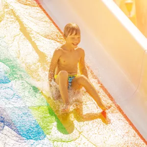 book-activites-2025-v8-enfant-qui-descends-un-toboggan-aquatique-couleur-arc-en-ciel-avec-le-sourire