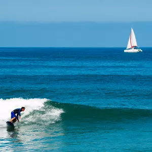 Surfeur avec au large un voilier par un mer d'huile avec quelques rouleaux.