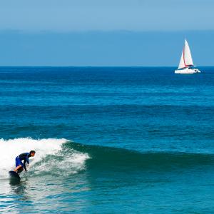 Surfeur avec au large un voilier par un mer d'huile avec quelques rouleaux.